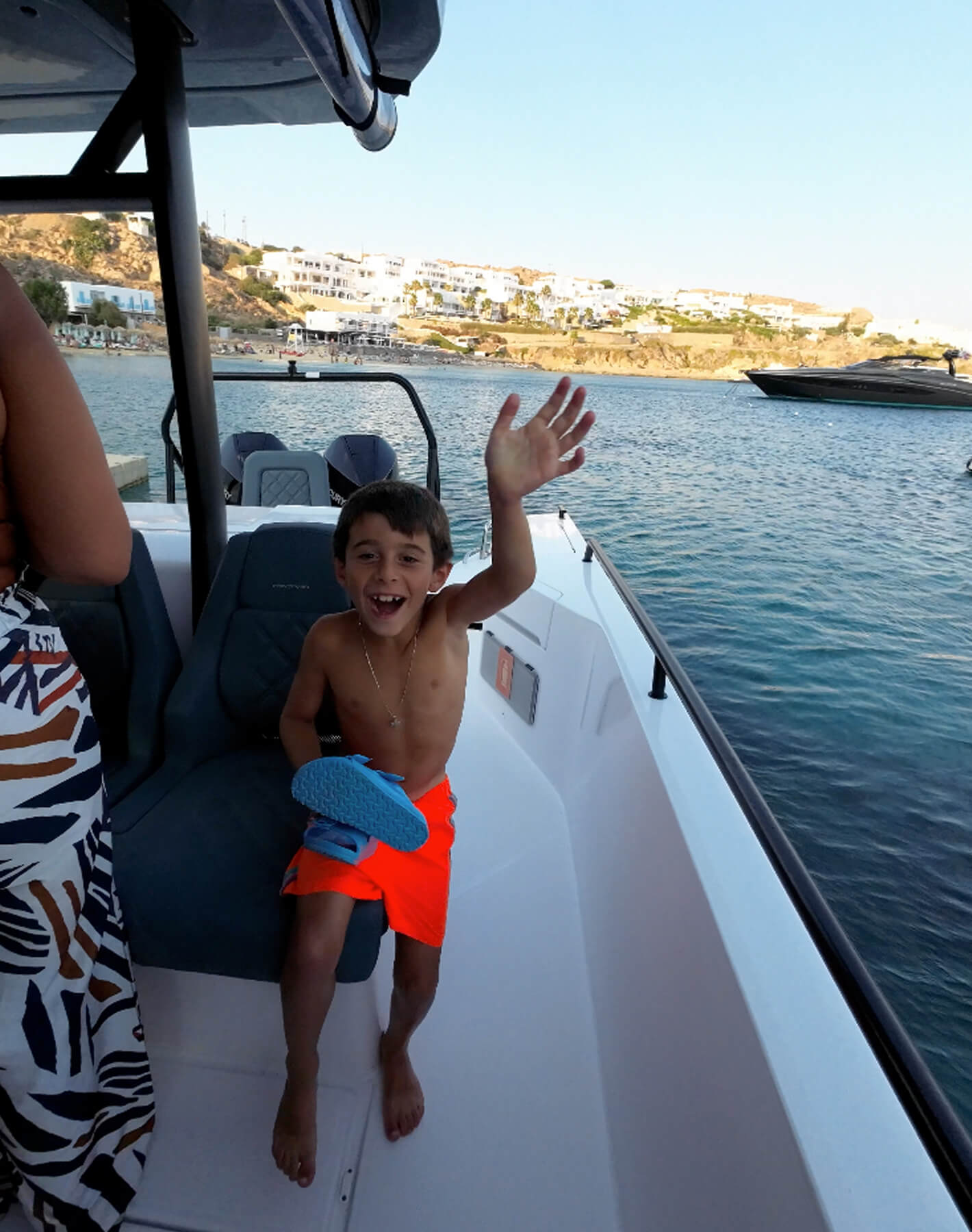 Pure joy in the Aegean: A happy boy waves from Cali's Axopar boat, surrounded by summer vibes among the Cycladic islands.