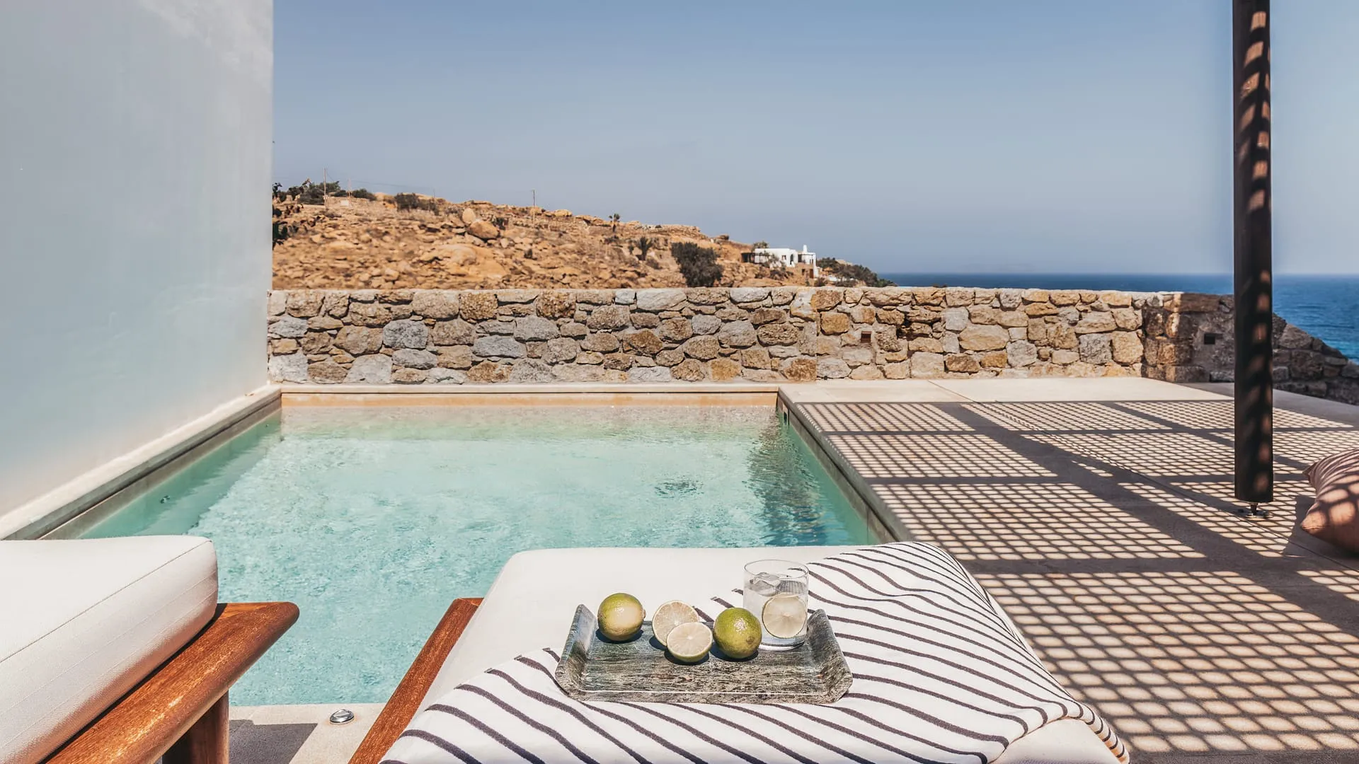 A private pool set into a stone terrace with two sunbeds, the bay and a bare hillside beyond
