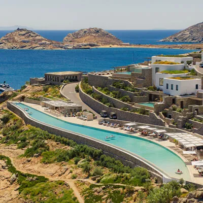 Drone shot of Cali Mykonos' infinity pool and its surroundings. Guests enjoying the pool, the loungers, the food and drink in the Greek summer sun.